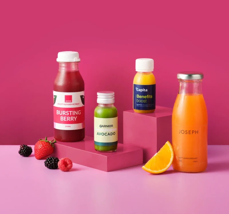 Custom branded juice shots and juice bottles against a pink background