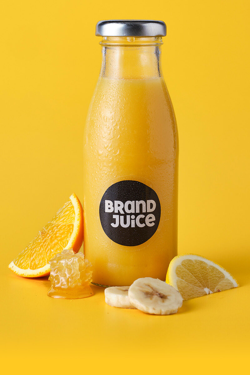 A bottle of custom branded orange juice with a clear label on a yellow background