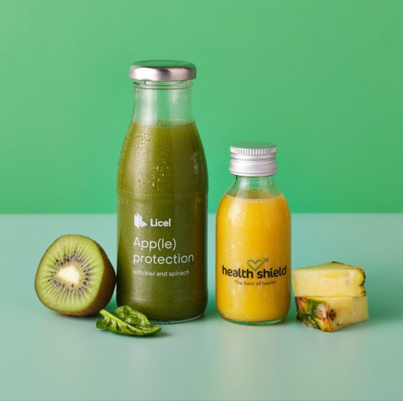 Two bottles of smoothies with the ingredients next to them on a green background