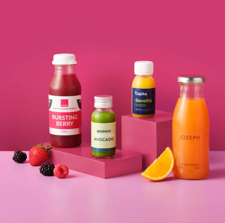 Several bottles of juice and juice shots on a pink background