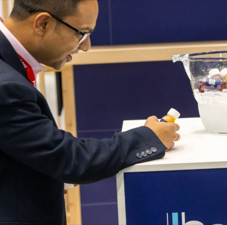 A man in a suit looking at a juice shot bottle at an exhibition event