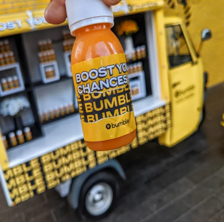 An orange juice shot with Bumble branding on with a drinks truck in the background