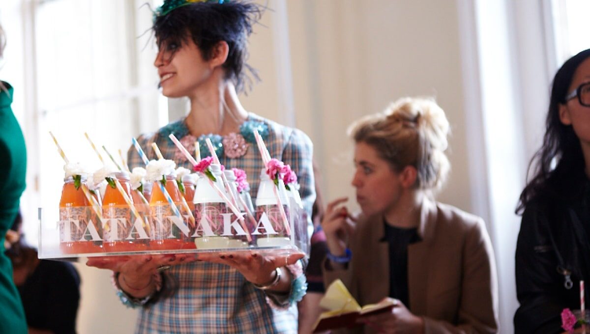 A tray of branded juice bottles being carried by a woman at an event