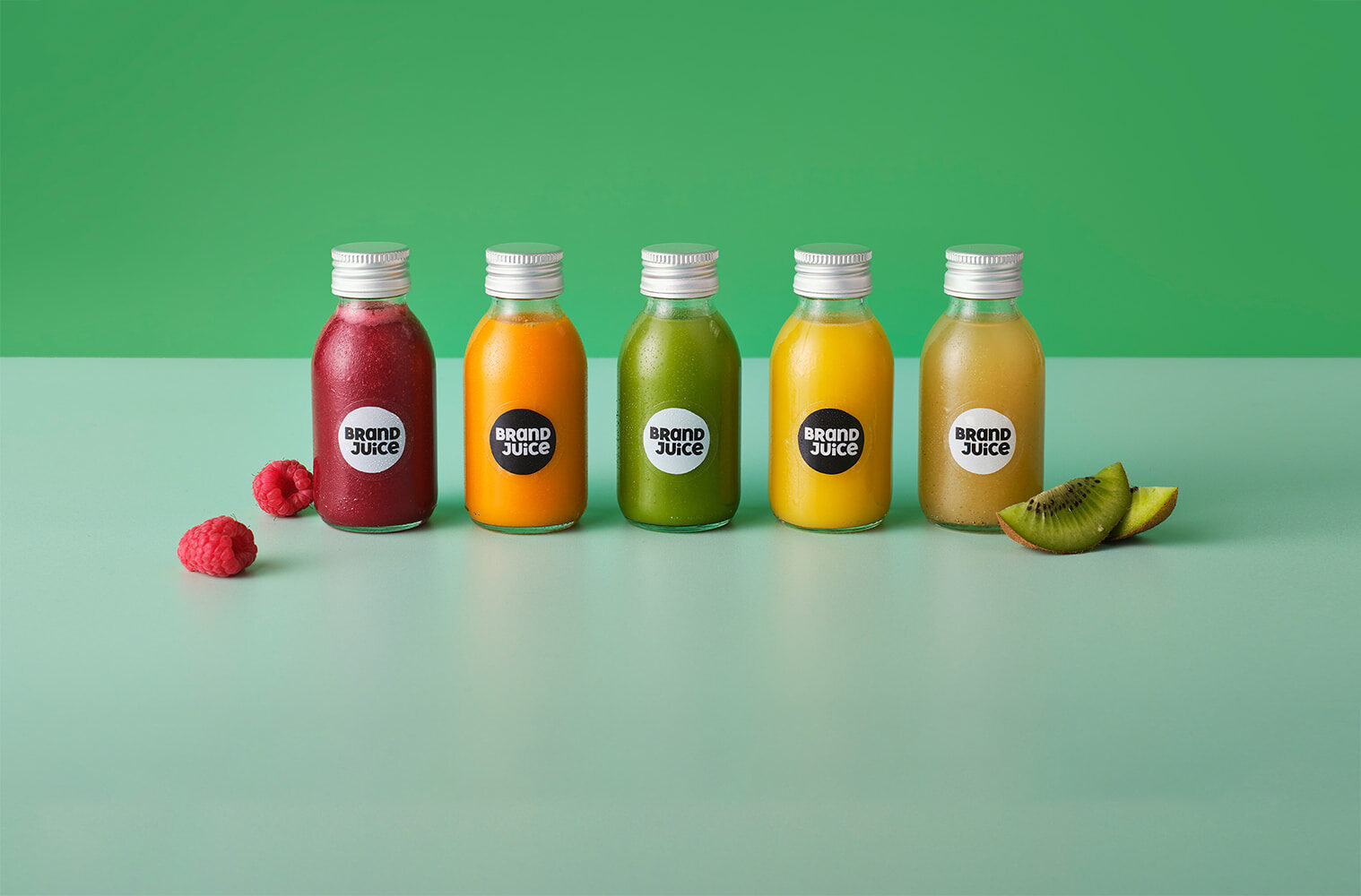 Five juice shot bottles with branded clear labels lined up against a green background