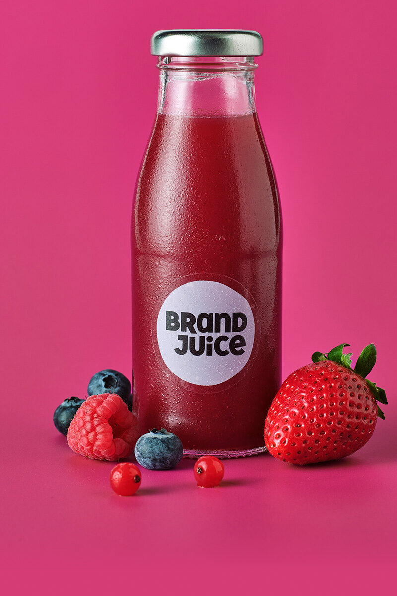 A glass bottle of red berry juice on a pink background