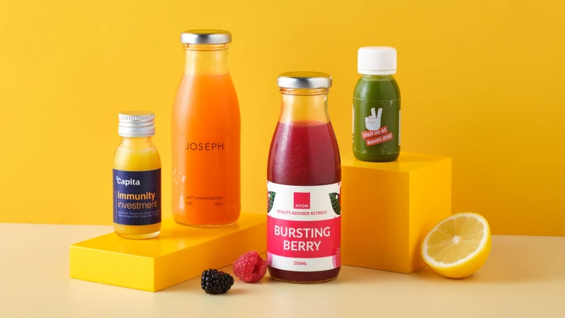 4 different sized juice bottled with fruit scattered